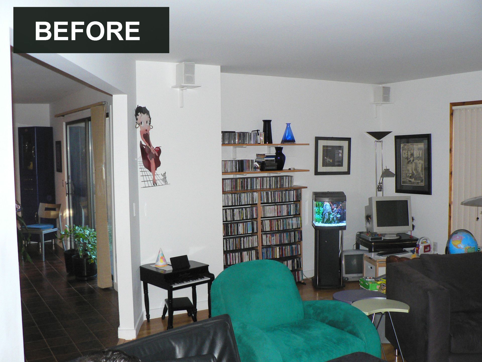 Living room before renovation: white walls, shelves with CDs, blue chair, aquarium, and dark furniture.