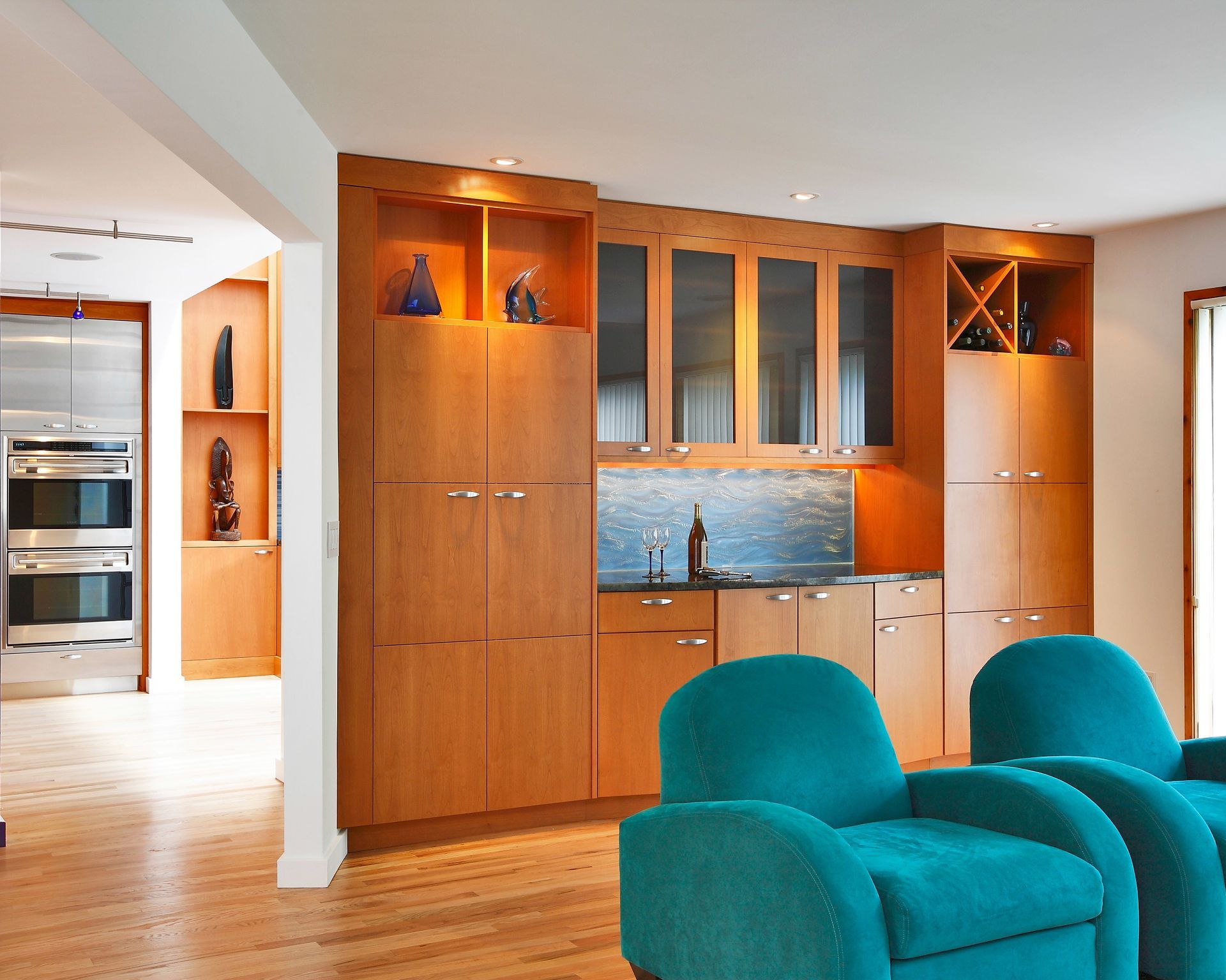 Wooden built-in bar with teal armchairs, featuring cabinets, a sink, and wine storage.