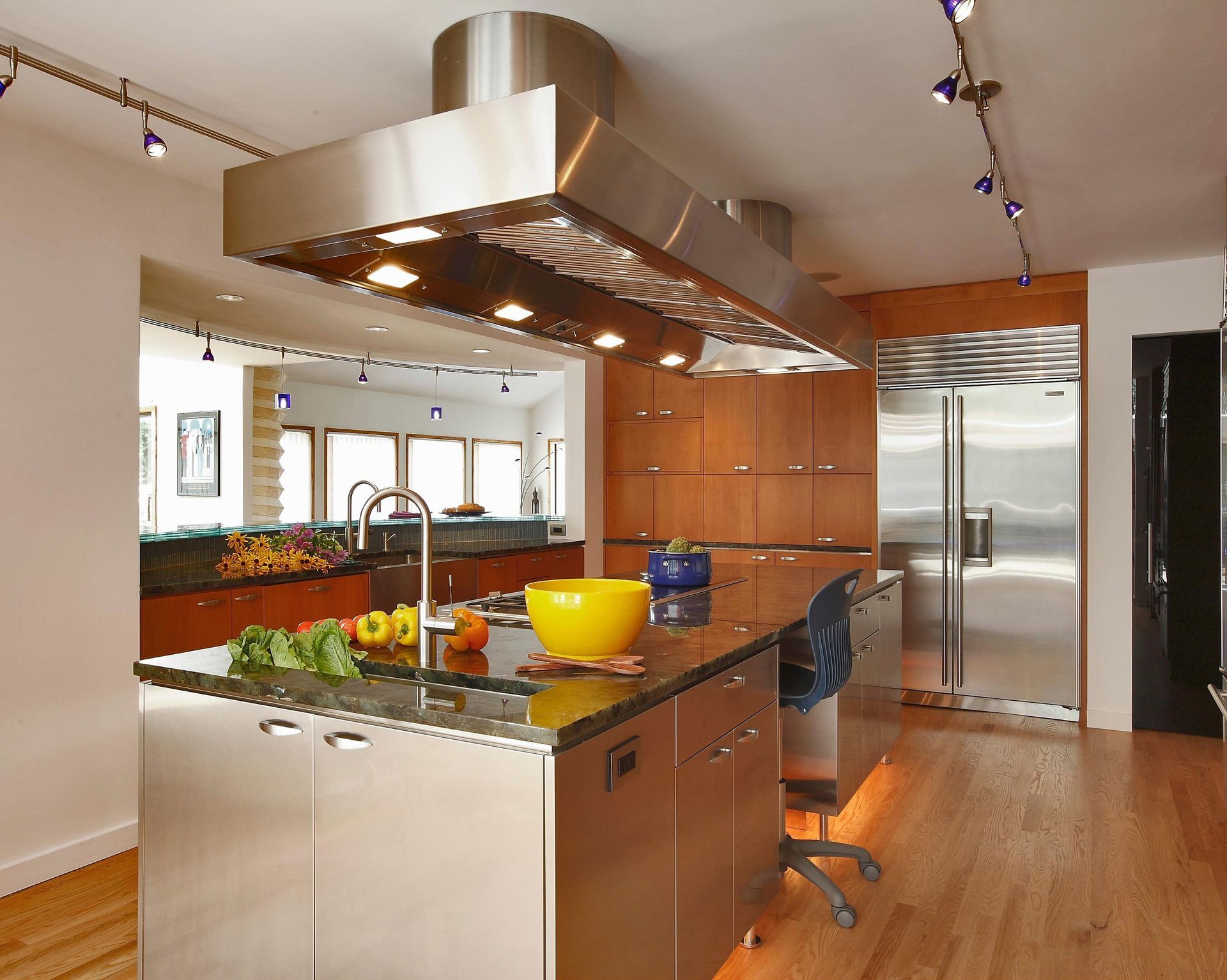 Modern kitchen with stainless steel island and range hood, wood cabinets, and track lighting.