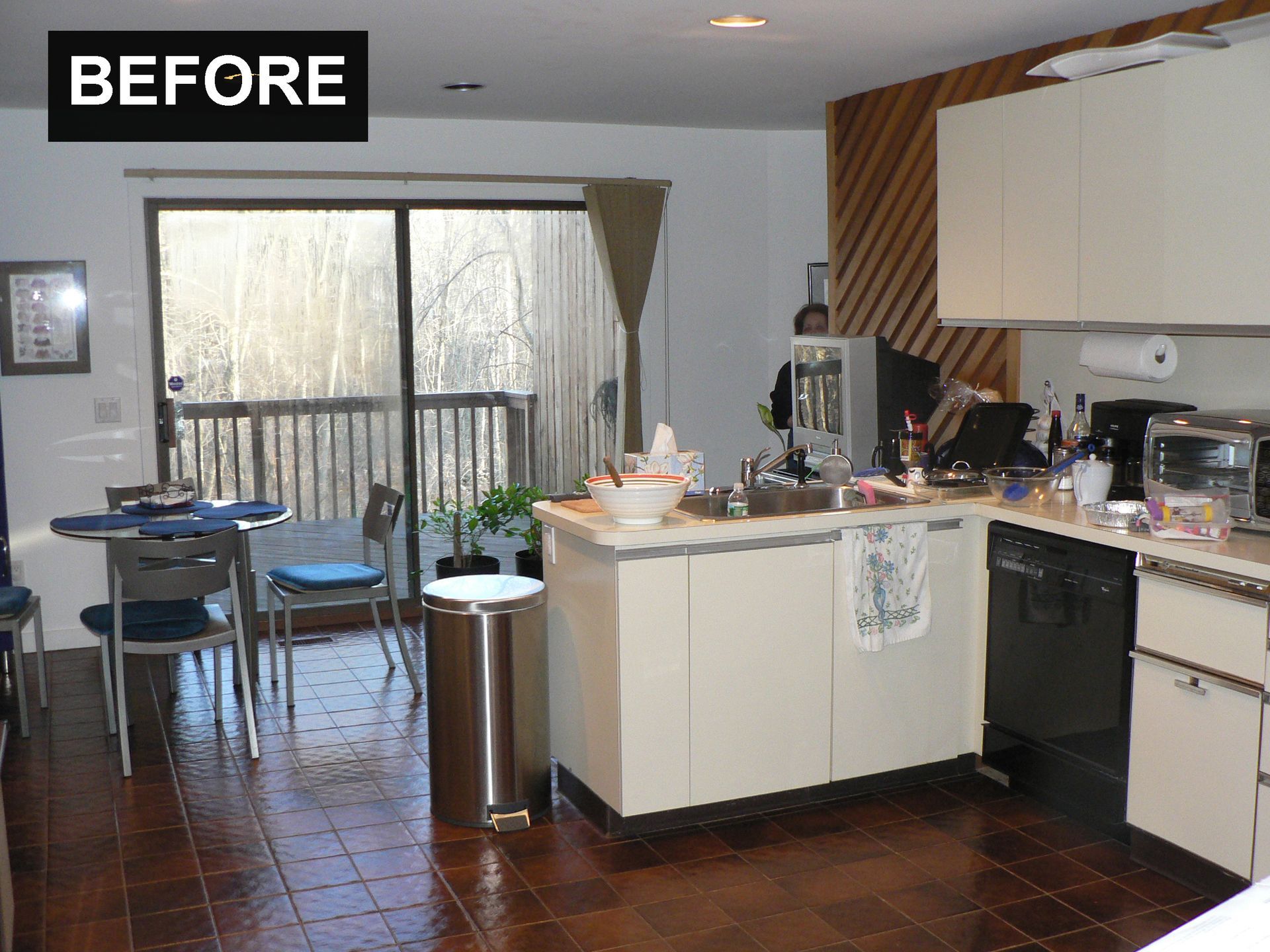 Kitchen before renovation: island, cabinets, appliances, table, chairs, sliding door, and dark tile floor.