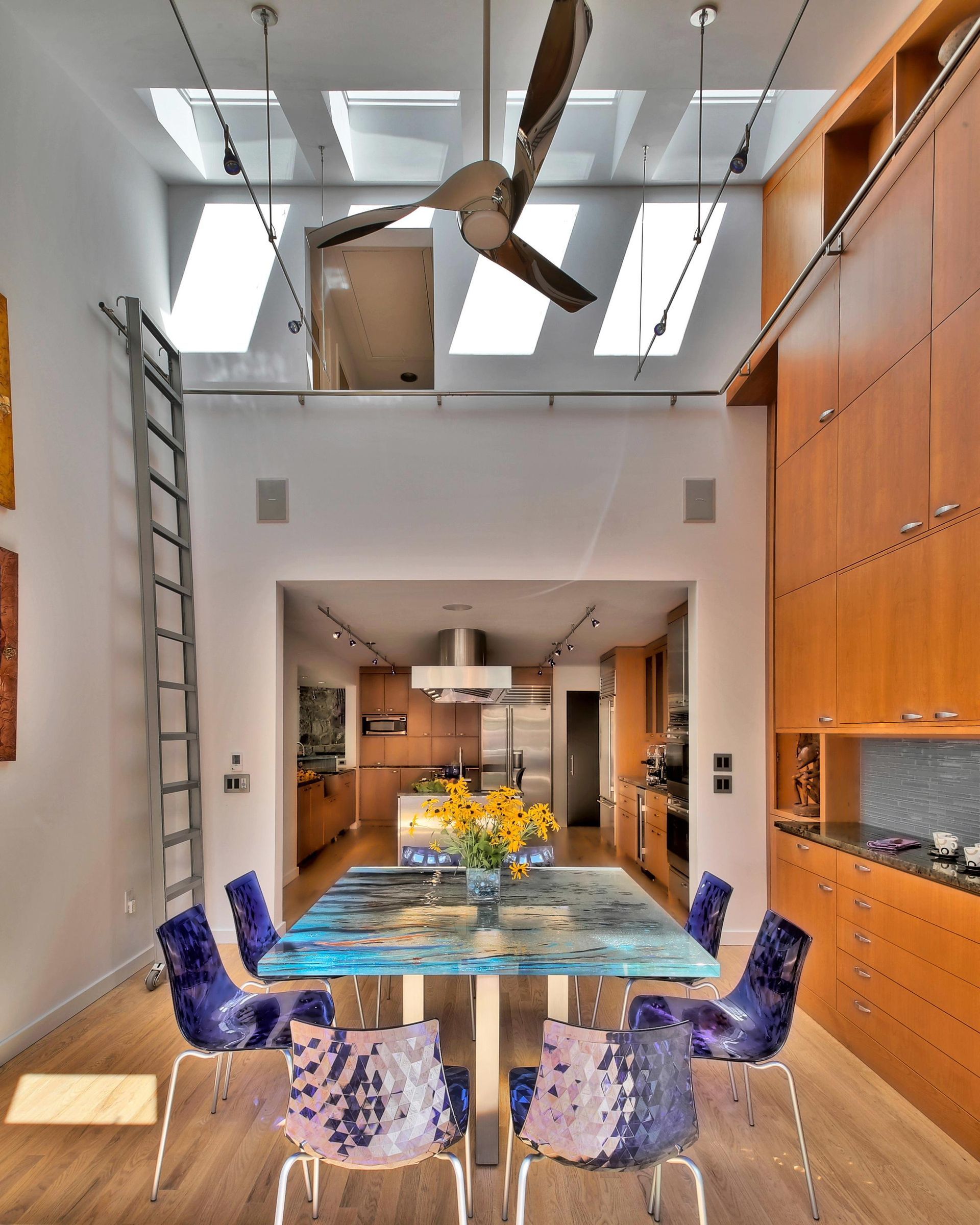 Dining room with blue table, purple chairs, and tall wooden cabinets. Skylights and a ladder are visible.