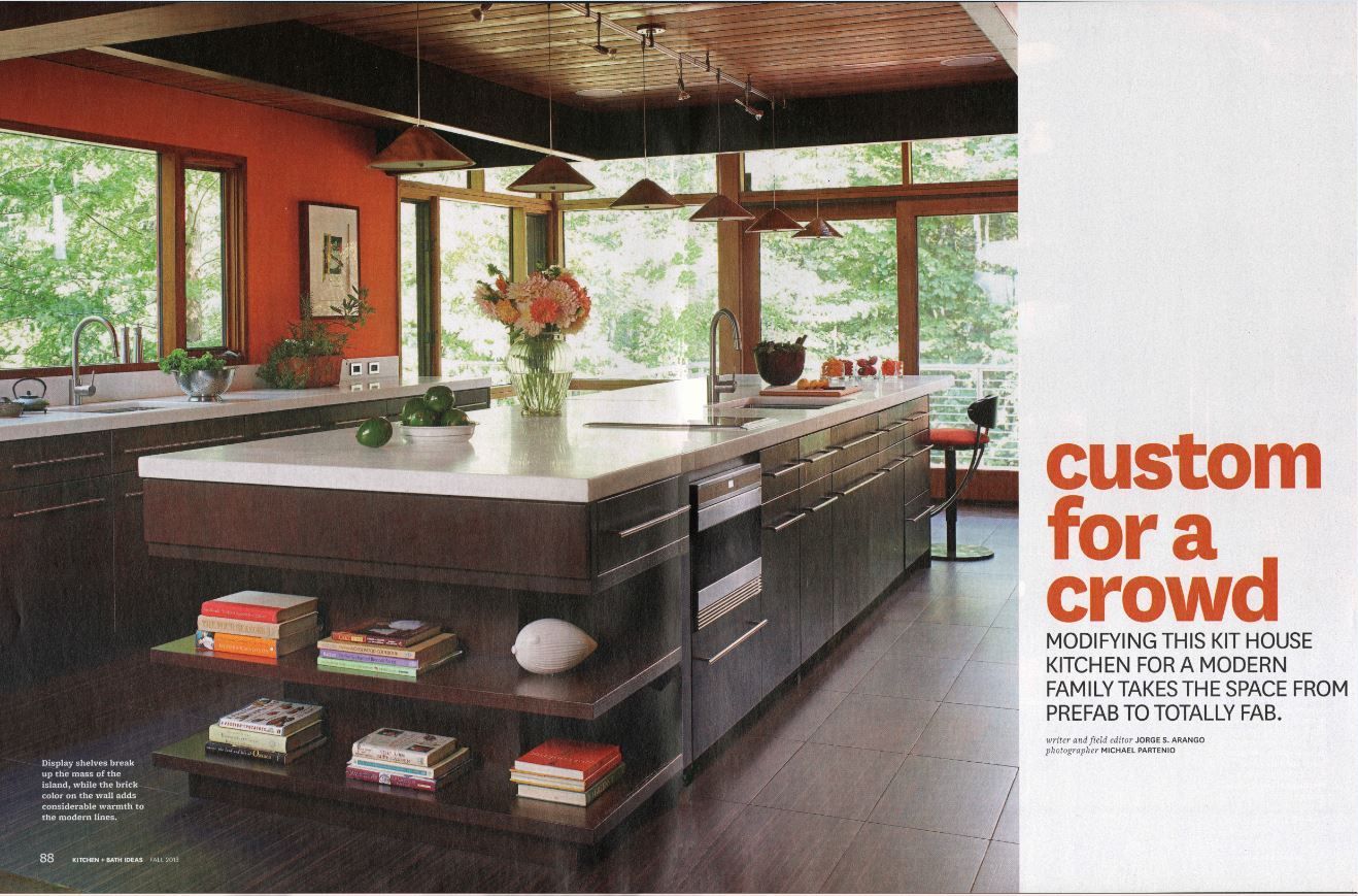 Modern kitchen with brown cabinets, large island, orange wall, and expansive windows.