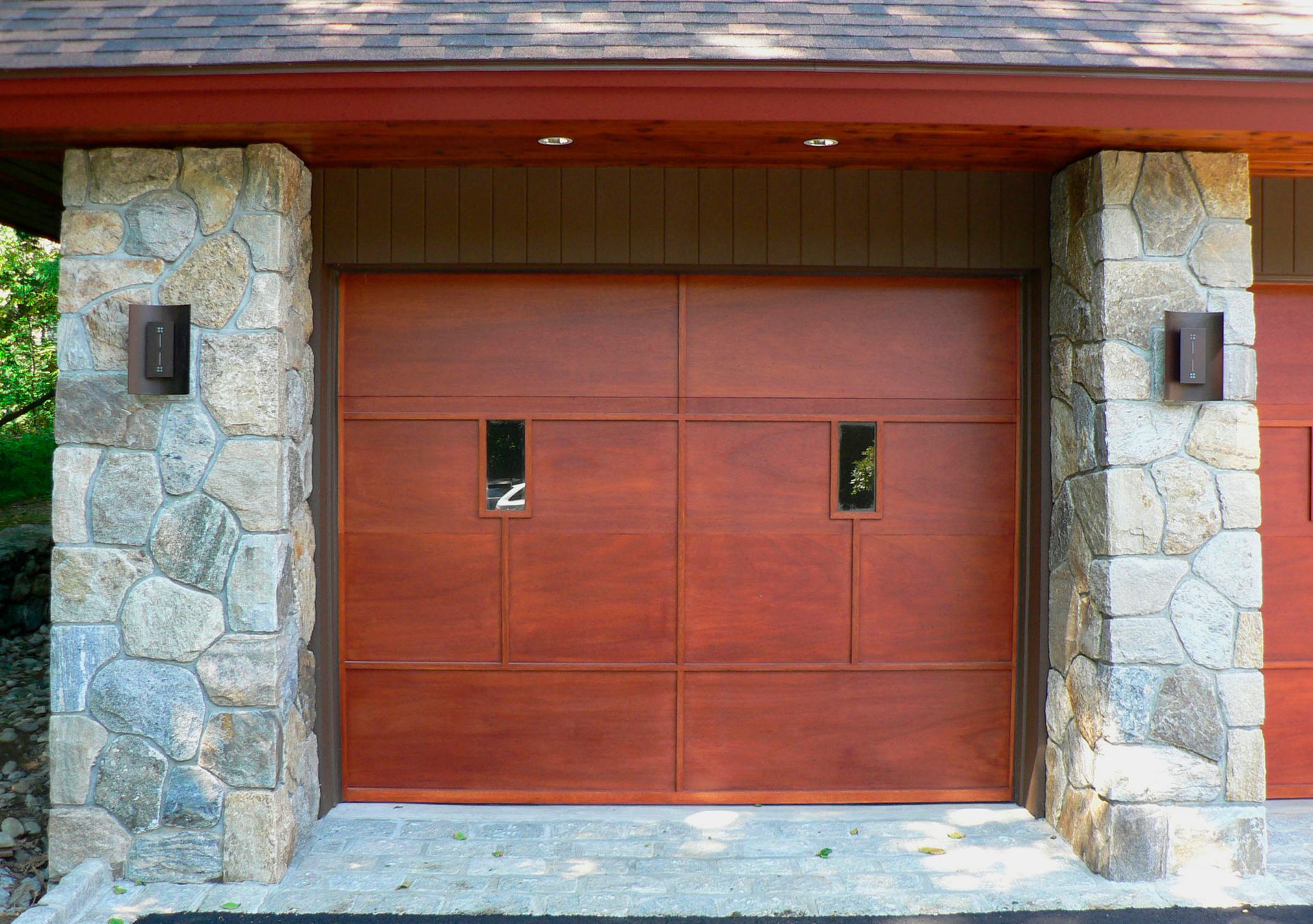 Wooden garage door with stone pillars, accented by sconces.