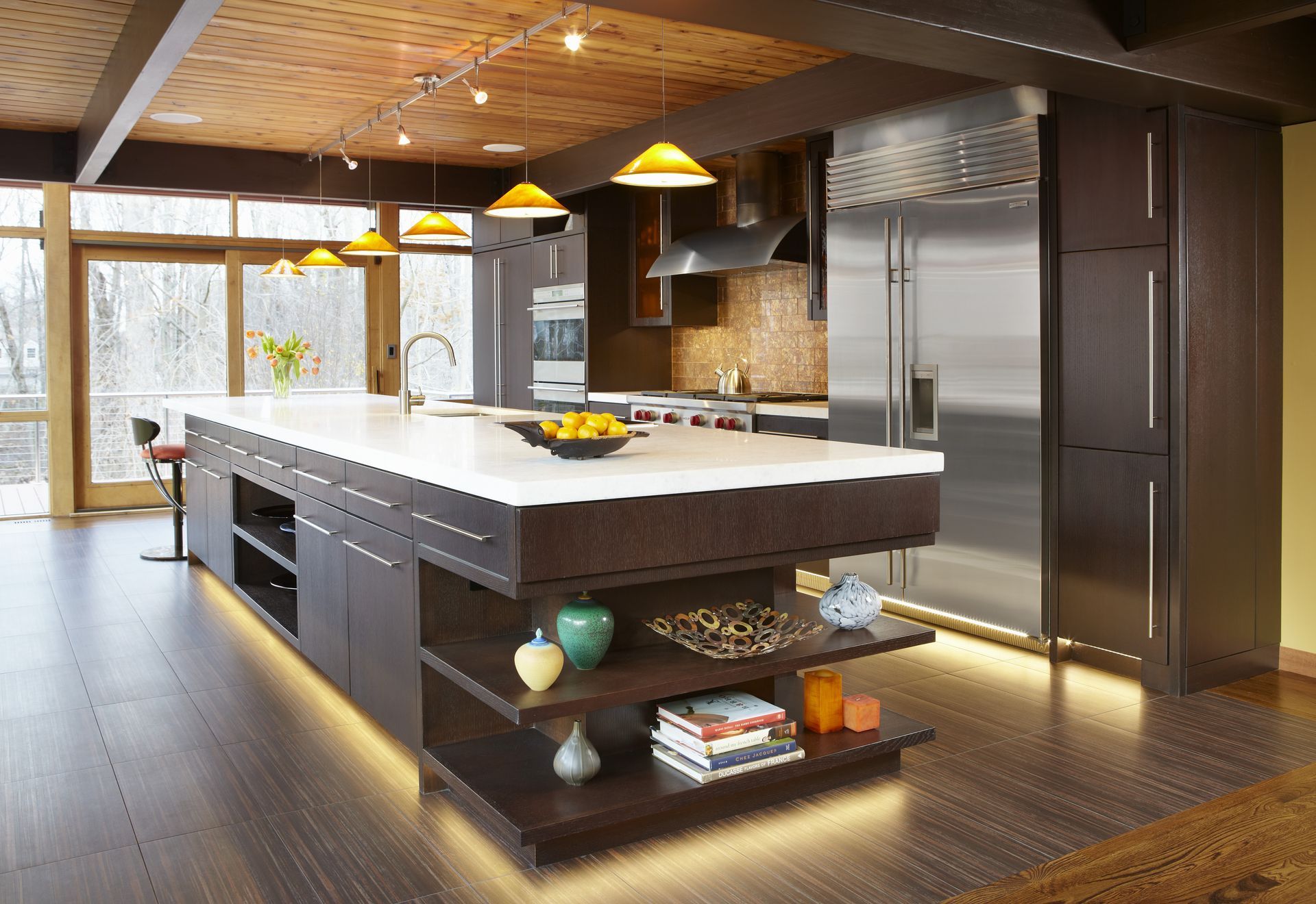 Modern kitchen with dark cabinetry, white countertop, island with open shelving, and wood ceiling.