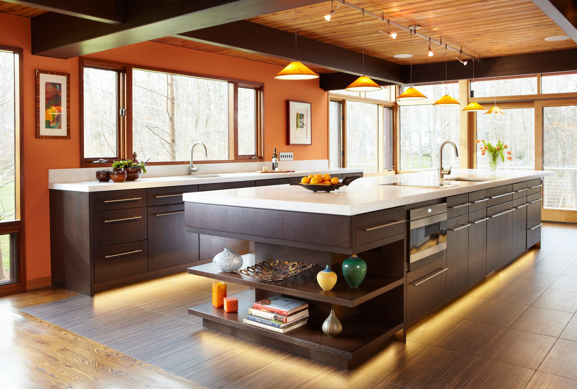 Modern kitchen with dark brown cabinets, large island, orange walls, and large windows.