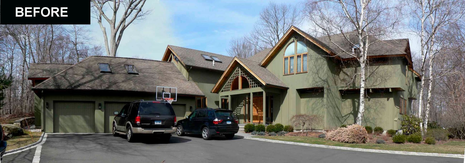 A two-story green house with a driveway. Two cars are parked outside the garage. The sky is blue.
