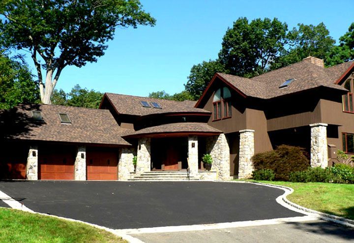 Brown house with brown shingle roof, three-car garage, stone columns, and asphalt driveway.