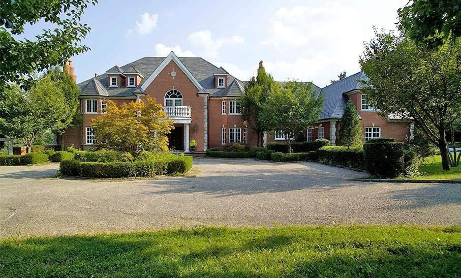 Brick mansion with a gray roof and circular driveway surrounded by trees and green grass.