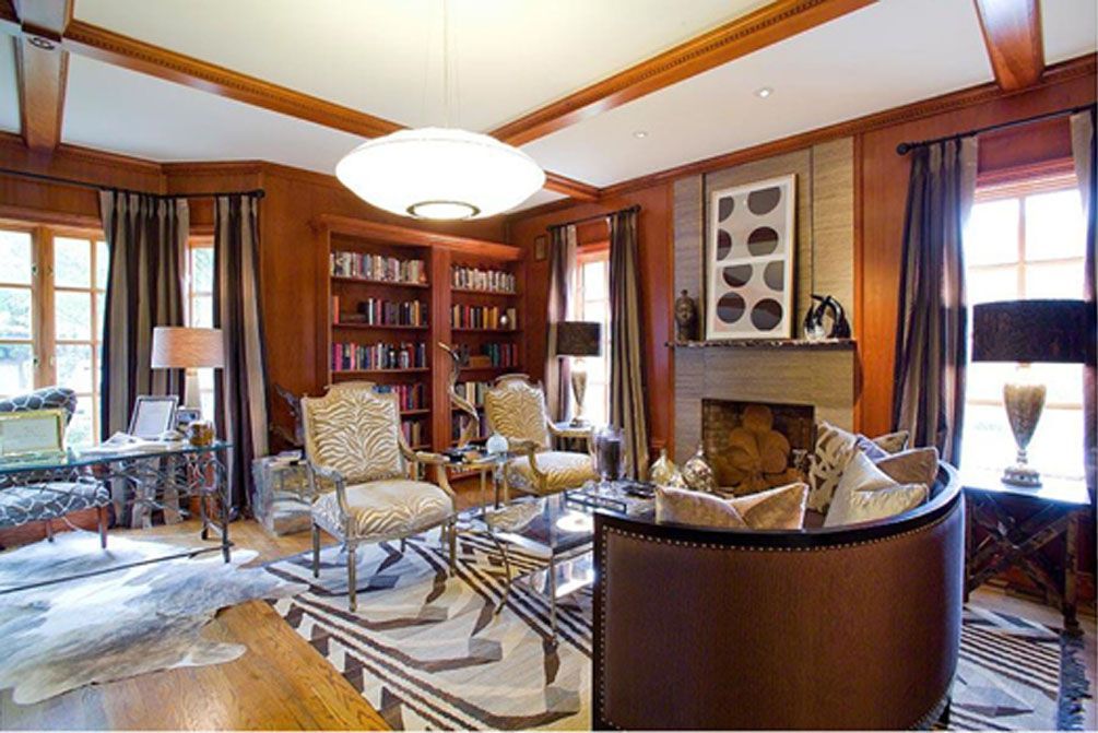 Luxurious living room with brown wood paneling, fireplace, bookshelves, and seating.