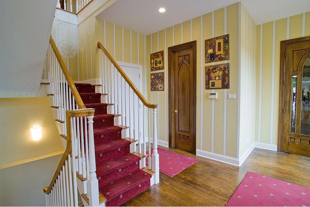 Staircase with red carpet, white banister, yellow striped walls, and wooden doors.