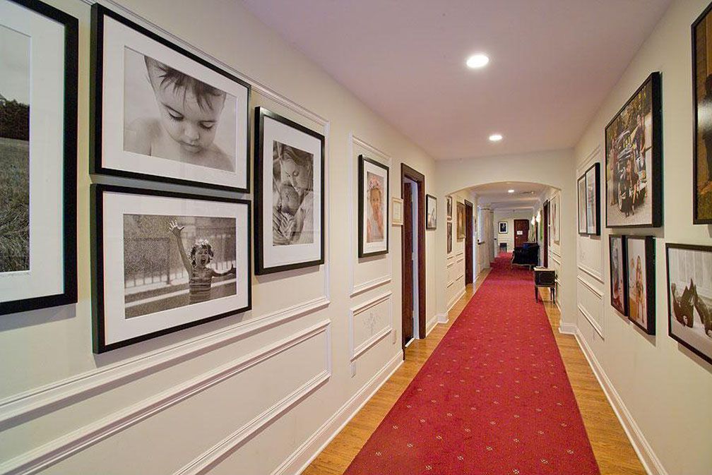 Hallway with red carpet, framed photos on walls, and recessed lighting.