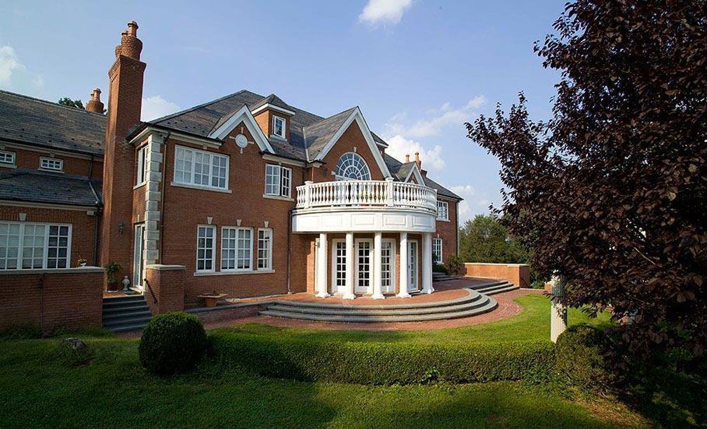 Red brick mansion with white trim, arched balcony, and manicured lawn.