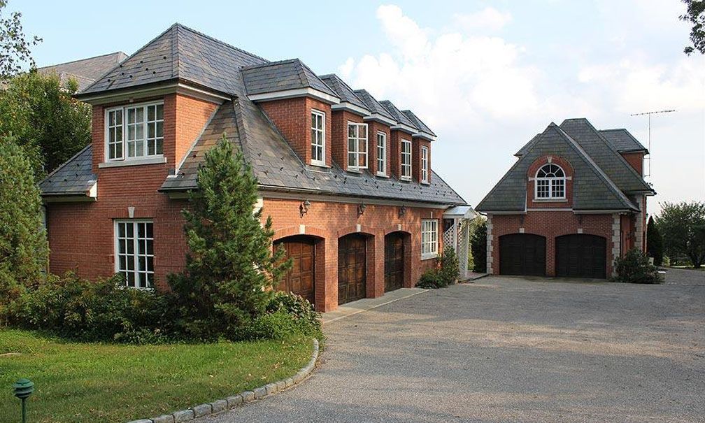 Red brick house with slate roof, arched garage doors, and a gravel driveway.