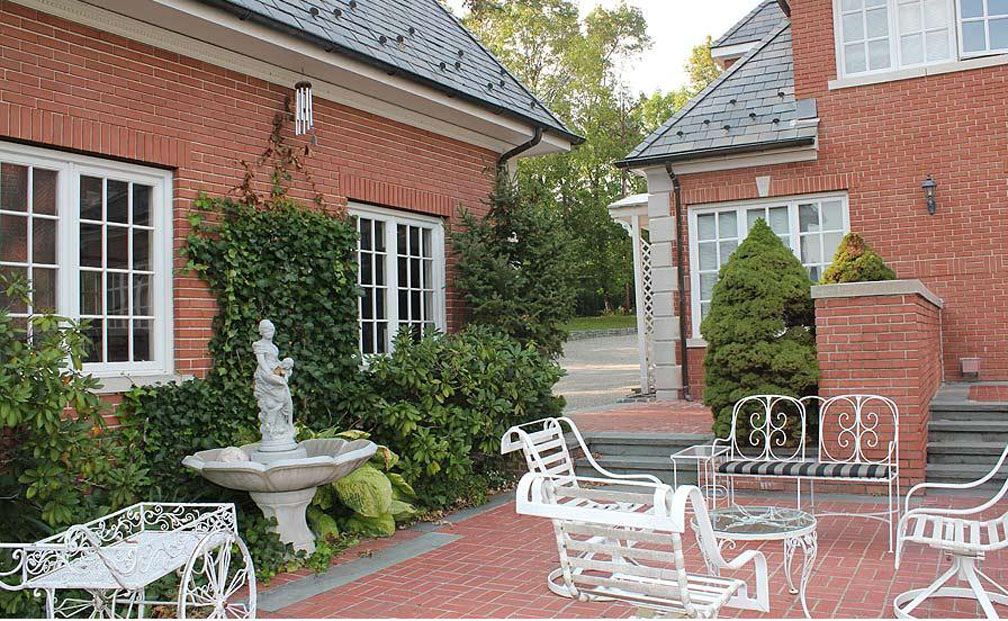Brick buildings with white-framed windows, a fountain, and white patio furniture on a brick patio.