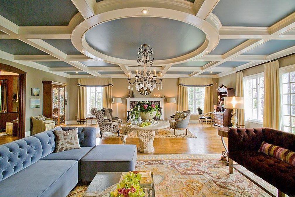 Luxurious living room with blue sectional sofa, chandelier, and coffered ceiling.