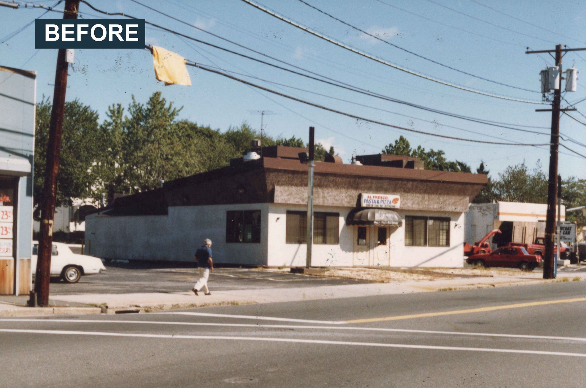 Before: A one-story white building with a dark roof on a corner lot. A person walks on the sidewalk.