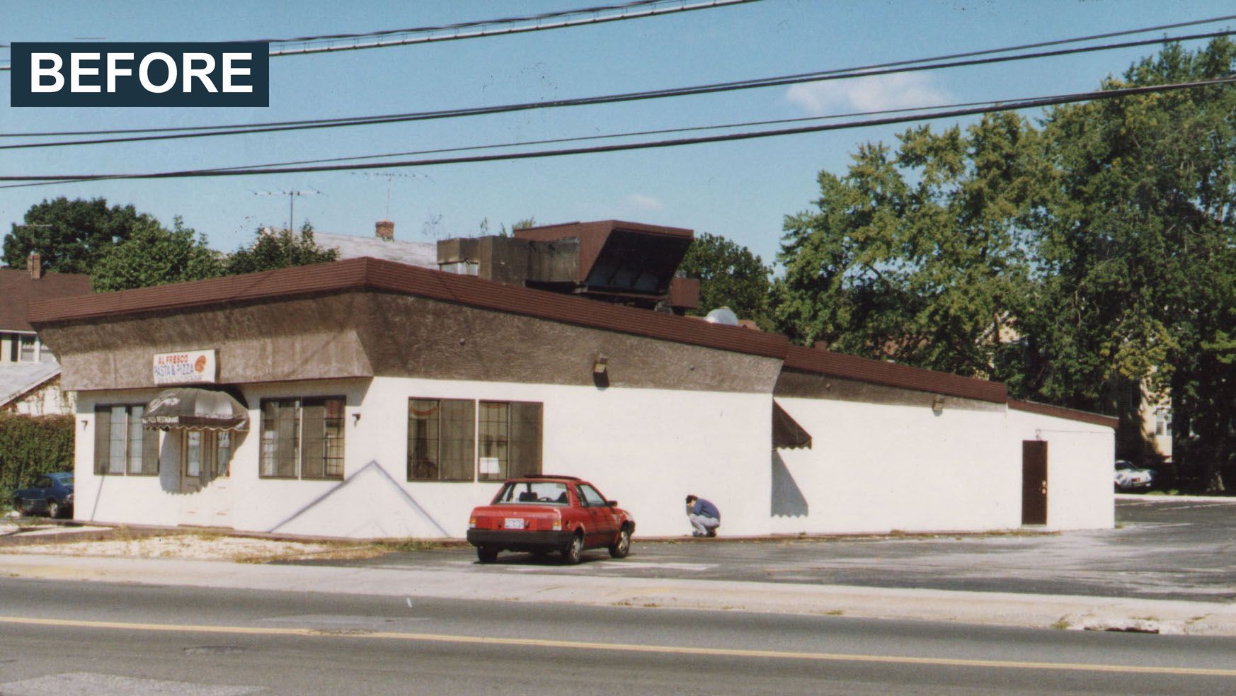 Exterior of a small white building with a brown roof and a red car parked out front.