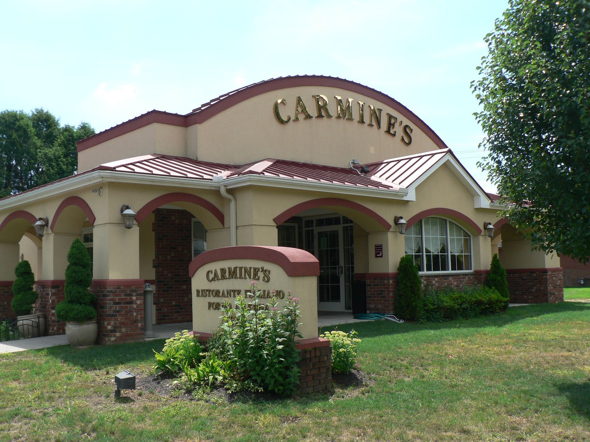 Carmine's restaurant, beige building with brown arched accents, sign, greenery, and blue sky.