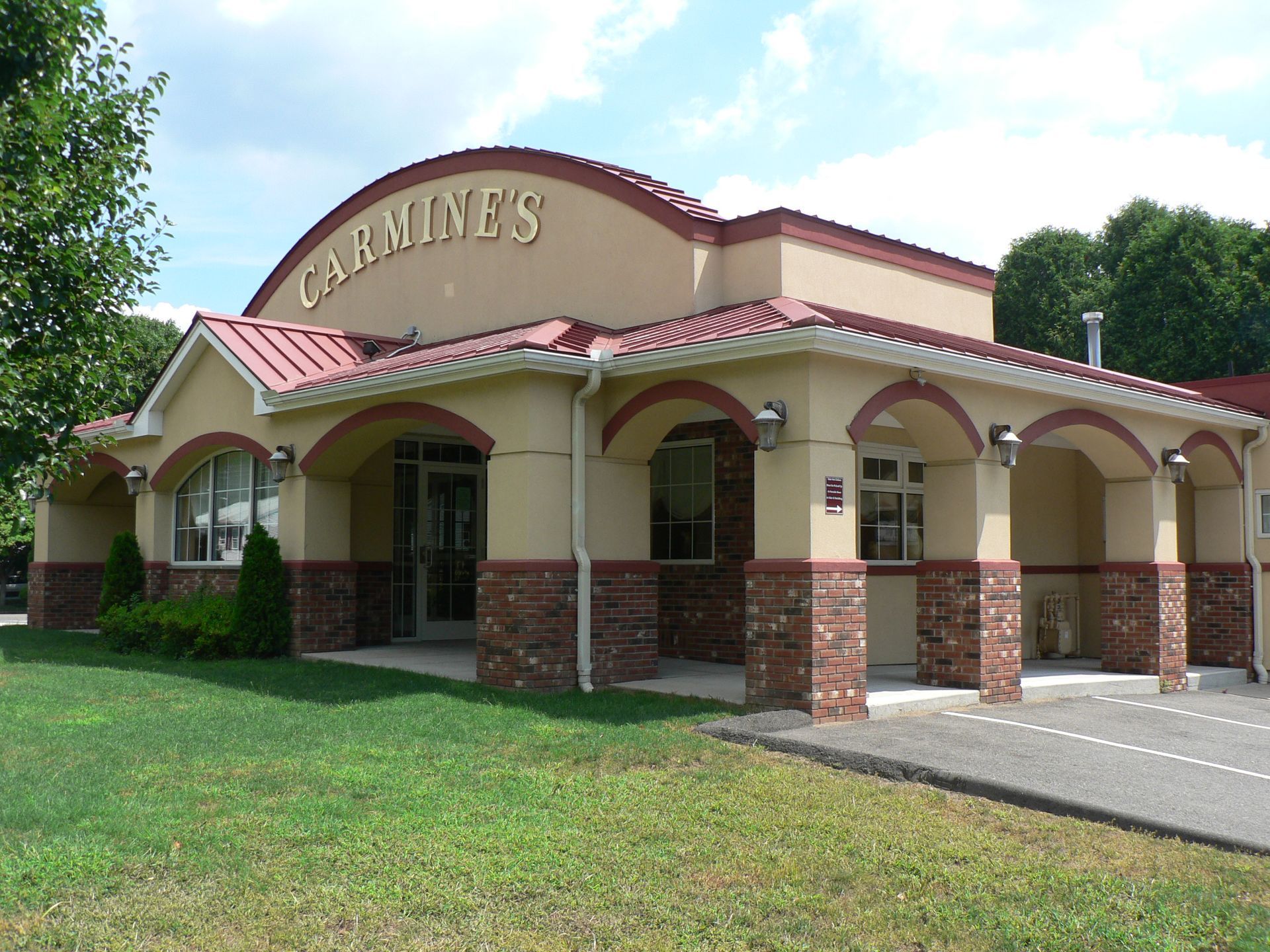 Carmine's restaurant, beige building with red trim, brick columns, arched windows, green lawn, blue sky.