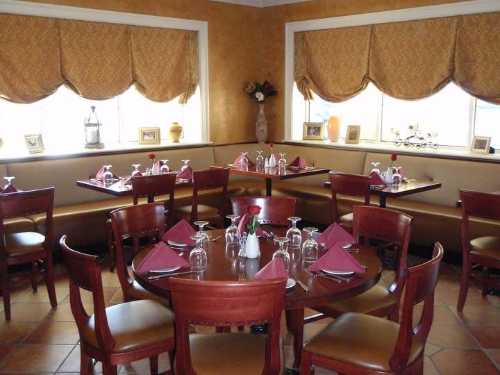 Restaurant interior with tables set for dining; windows with draped curtains.
