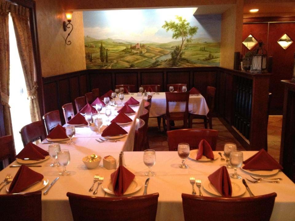 Formal dining room with long table set for a meal; red napkins, white tablecloth, mural background.