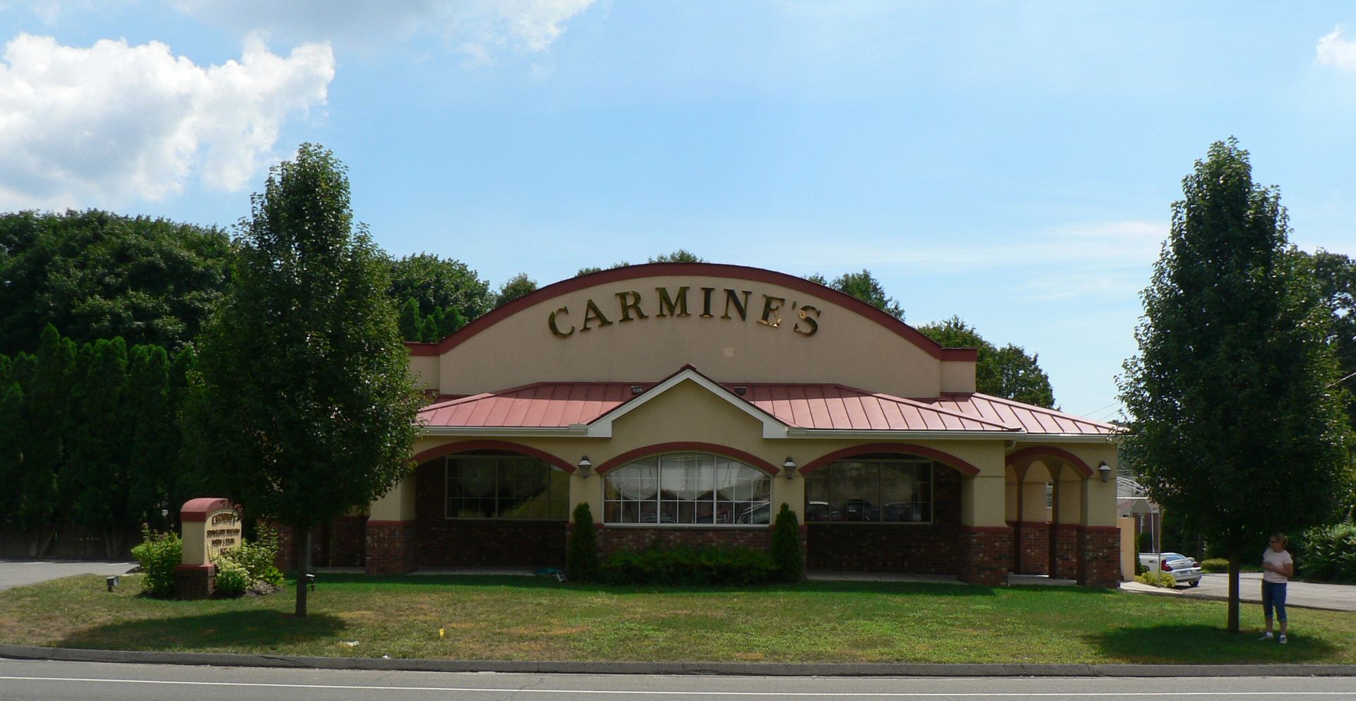Carmine's restaurant, tan building with red roof, arched sign, trees, blue sky.
