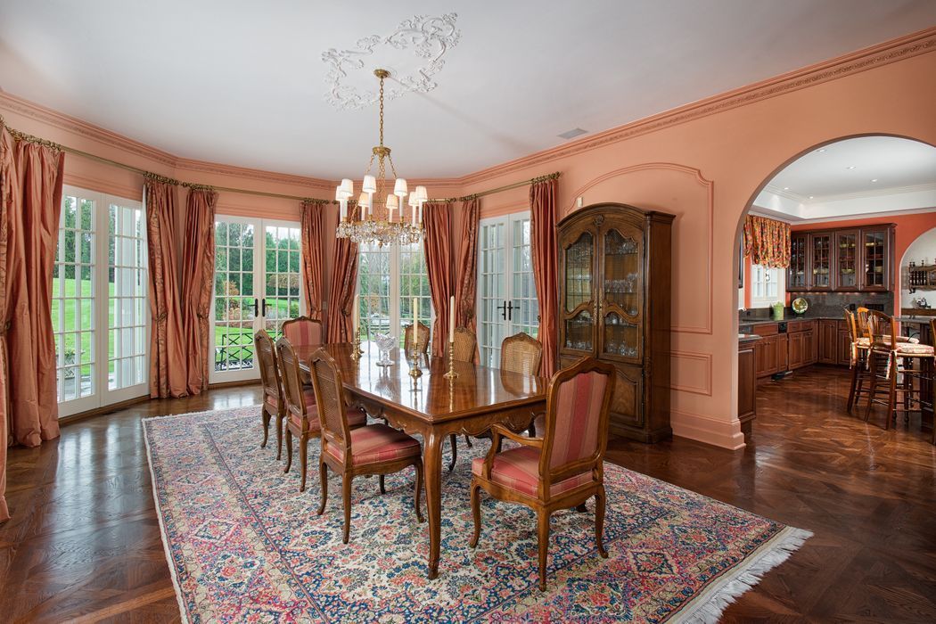 Elegant dining room with large table and chairs, large rug, arched doorways, and tall windows with pink curtains.