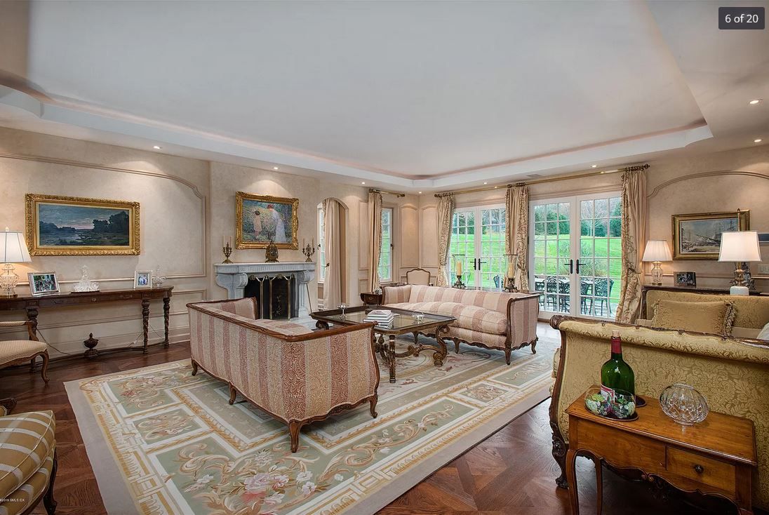 Elegant living room with antique furniture, large rug, and artwork. Natural light floods the space through large windows.