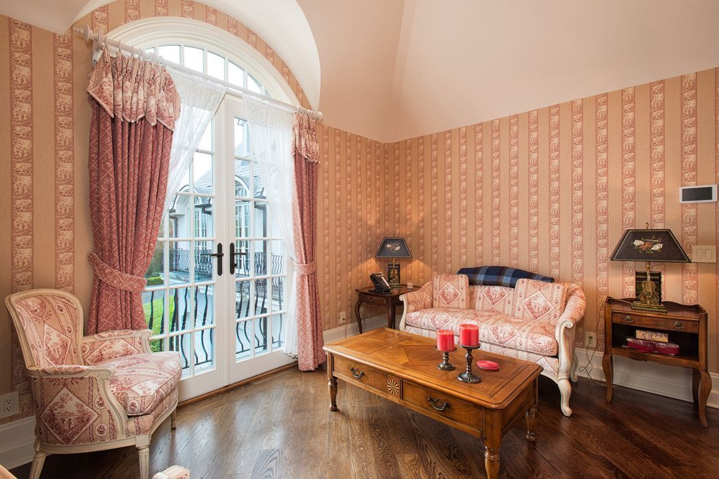 Living room with pink patterned wallpaper, ornate furniture, and French doors.