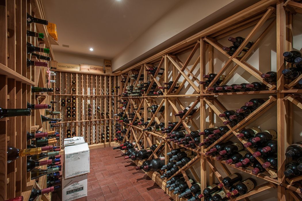Wine cellar with wooden racks filled with bottles, on red-tiled floor.