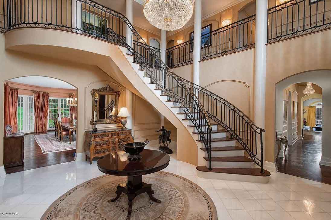 Elegant foyer with curved staircase, marble floors, and chandelier.