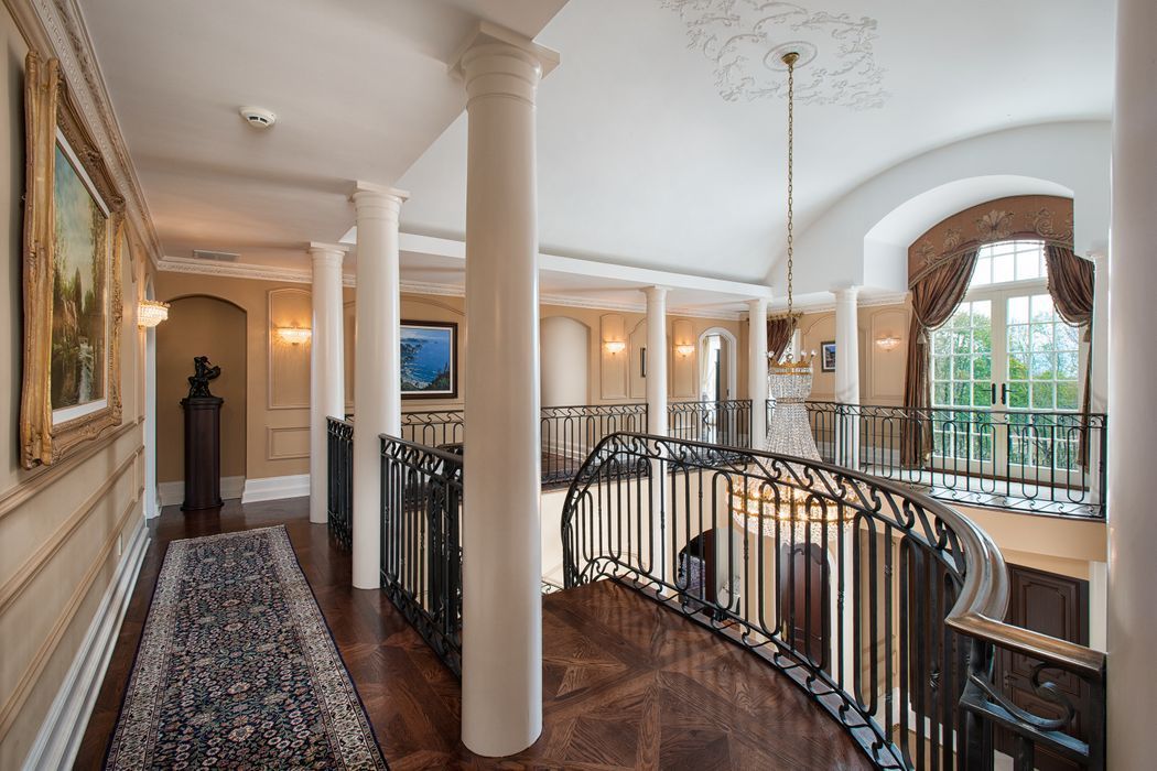 Hallway with ornate railing, columns, artwork, and large arched window.