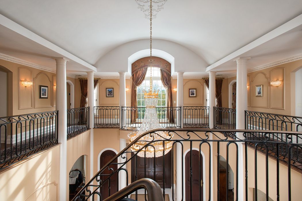 Grand foyer with curved ceiling, wrought iron balconies, chandelier, arched windows, and beige walls.