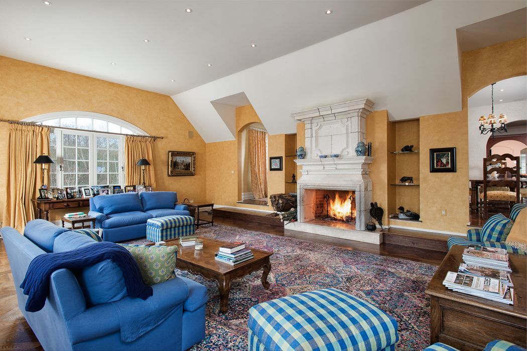 Living room with blue sofas, fireplace, and arched windows. Yellow walls and patterned rug.