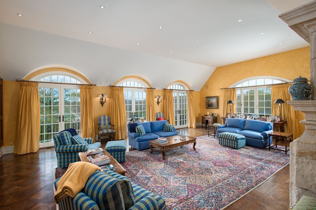 Spacious living room with blue sofas, patterned rug, and arched windows with yellow drapes and walls.