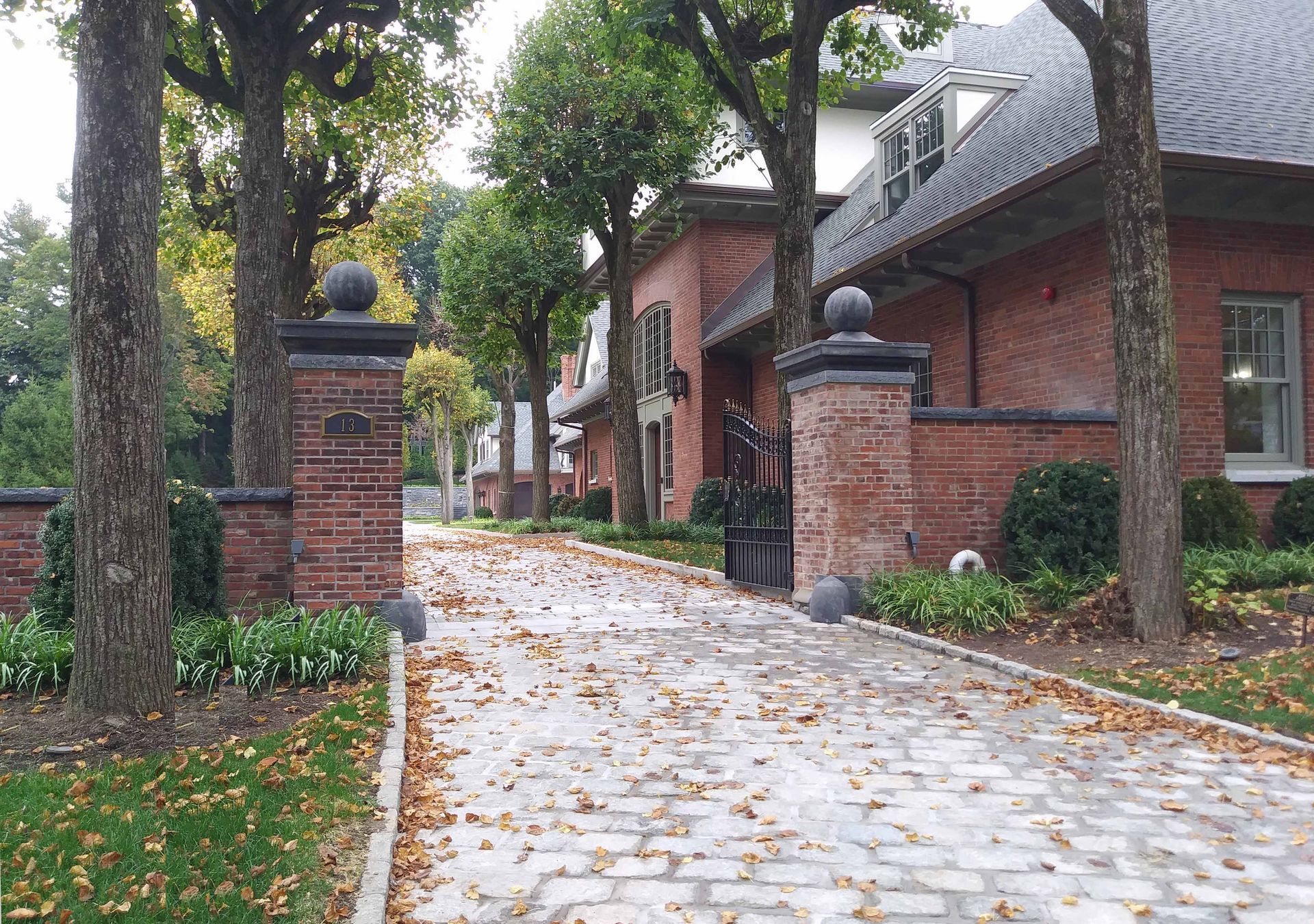 Brick driveway leading to a red brick building, trees on either side, fallen leaves.