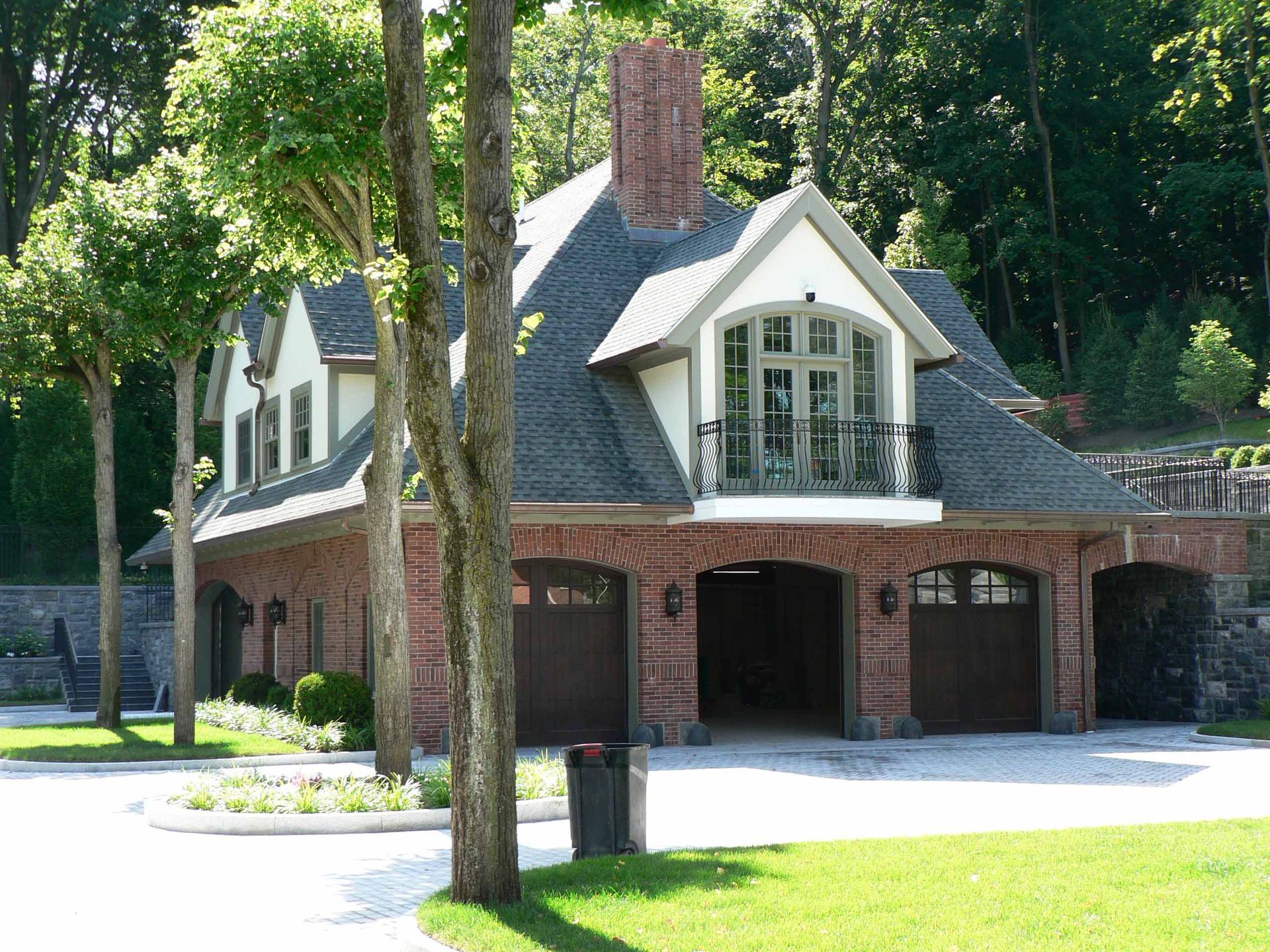 Brick garage with brown doors and green window, topped with a gray roof and tall chimney.
