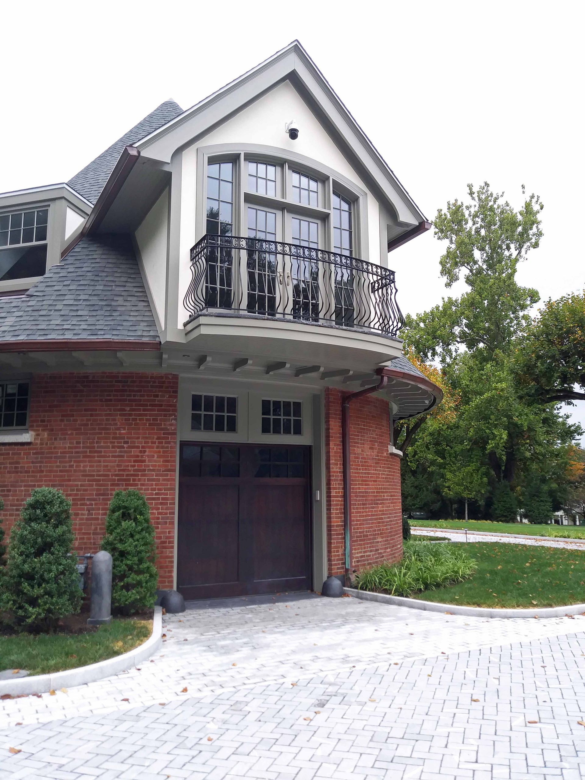 Brick building with a curved driveway, balcony, and dark wooden garage door.