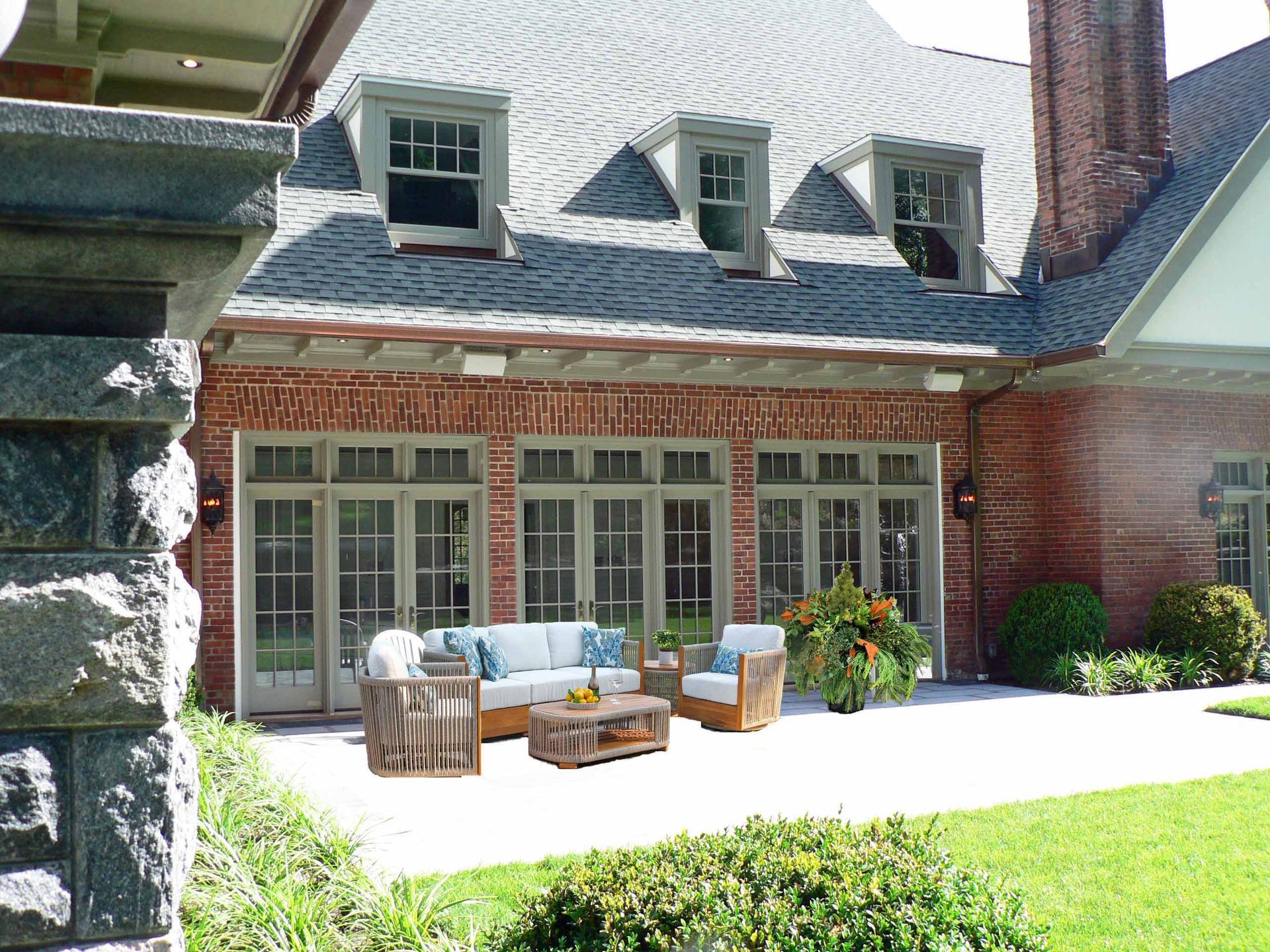 Patio with outdoor furniture next to a brick house. Sunny day, green grass, and blue cushions.
