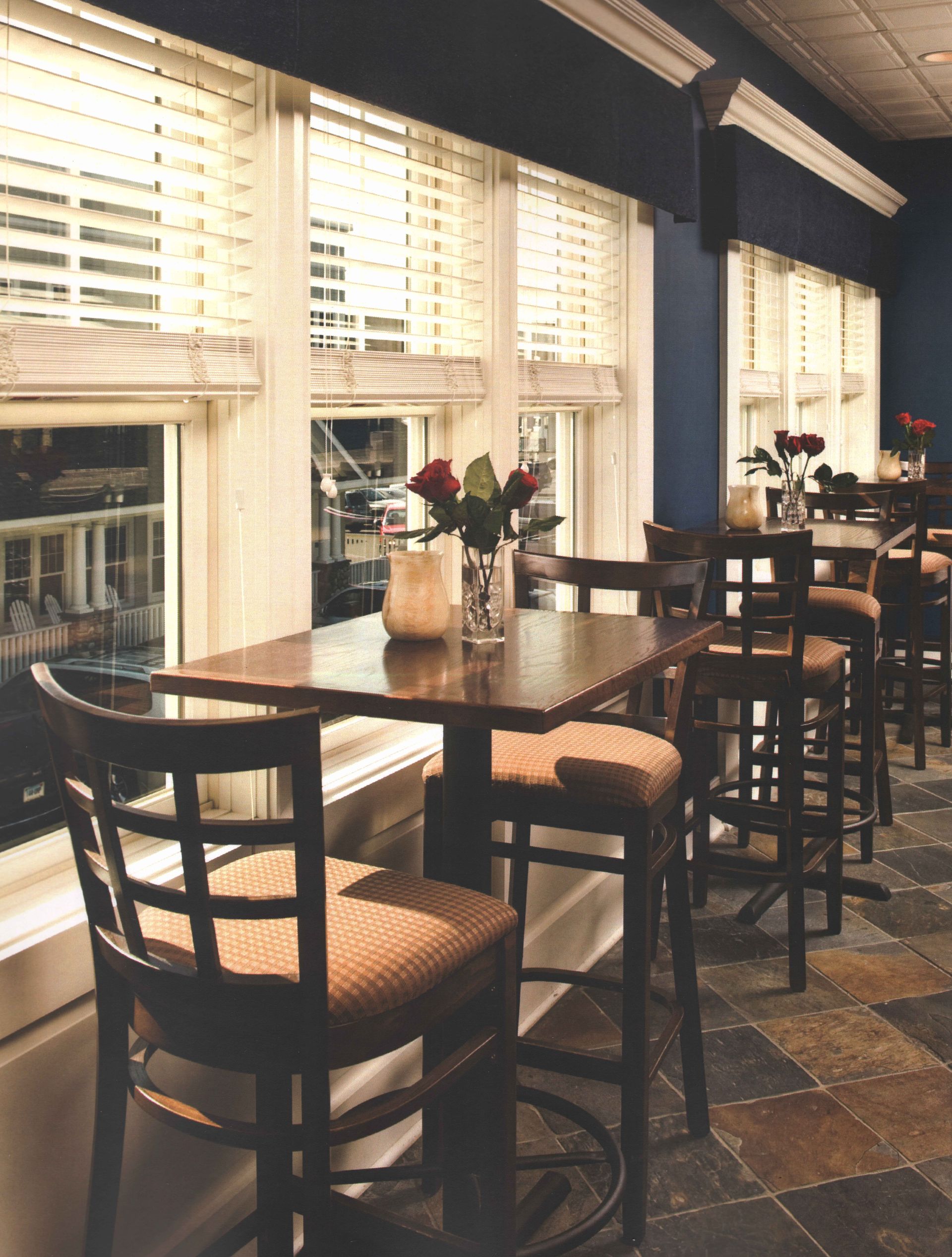 Restaurant interior with tables, chairs, and window seating. Dark blue walls and slate tile flooring.