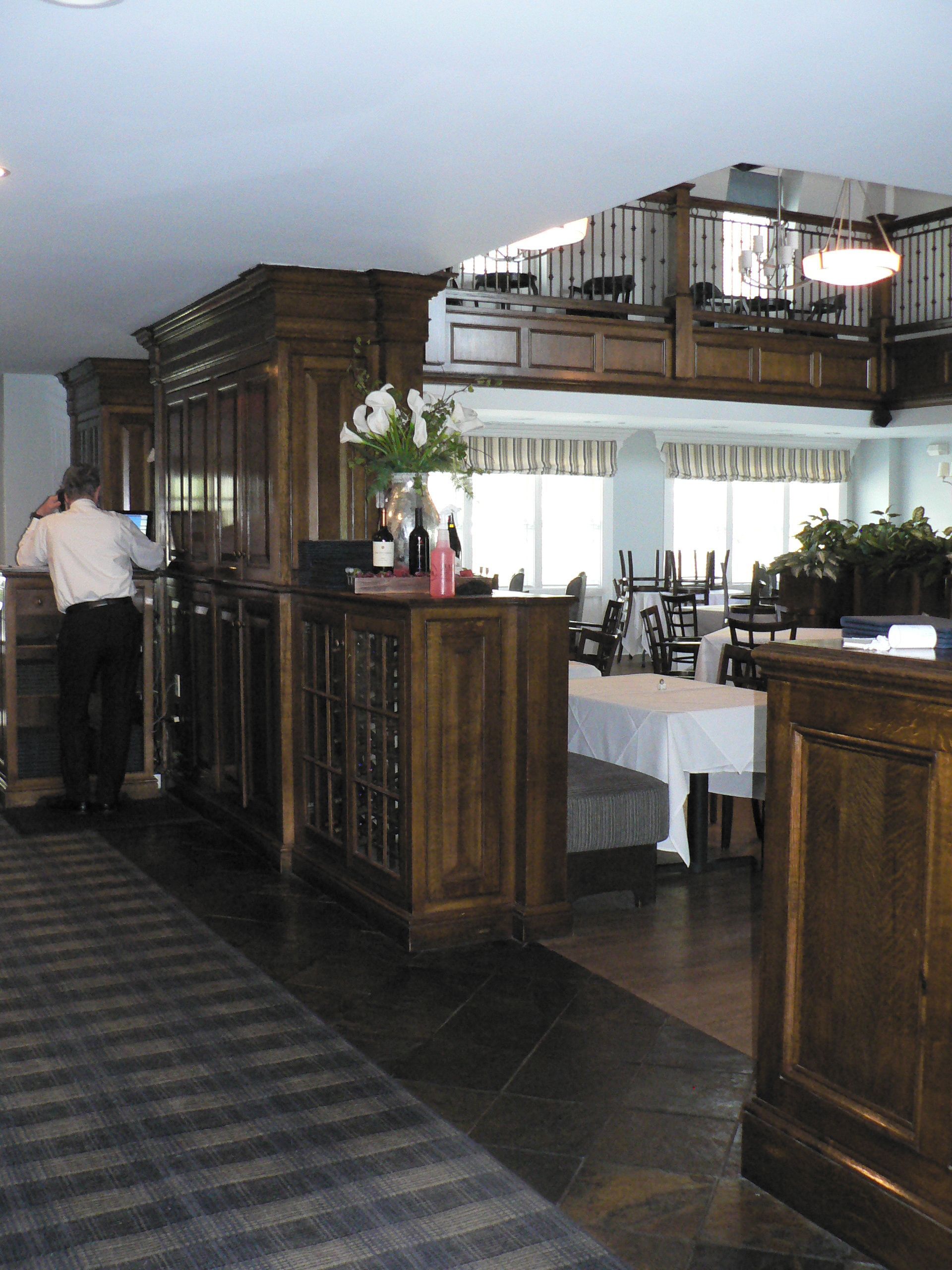 Restaurant interior with dark wood features and a person at a counter, leading to a dining area.