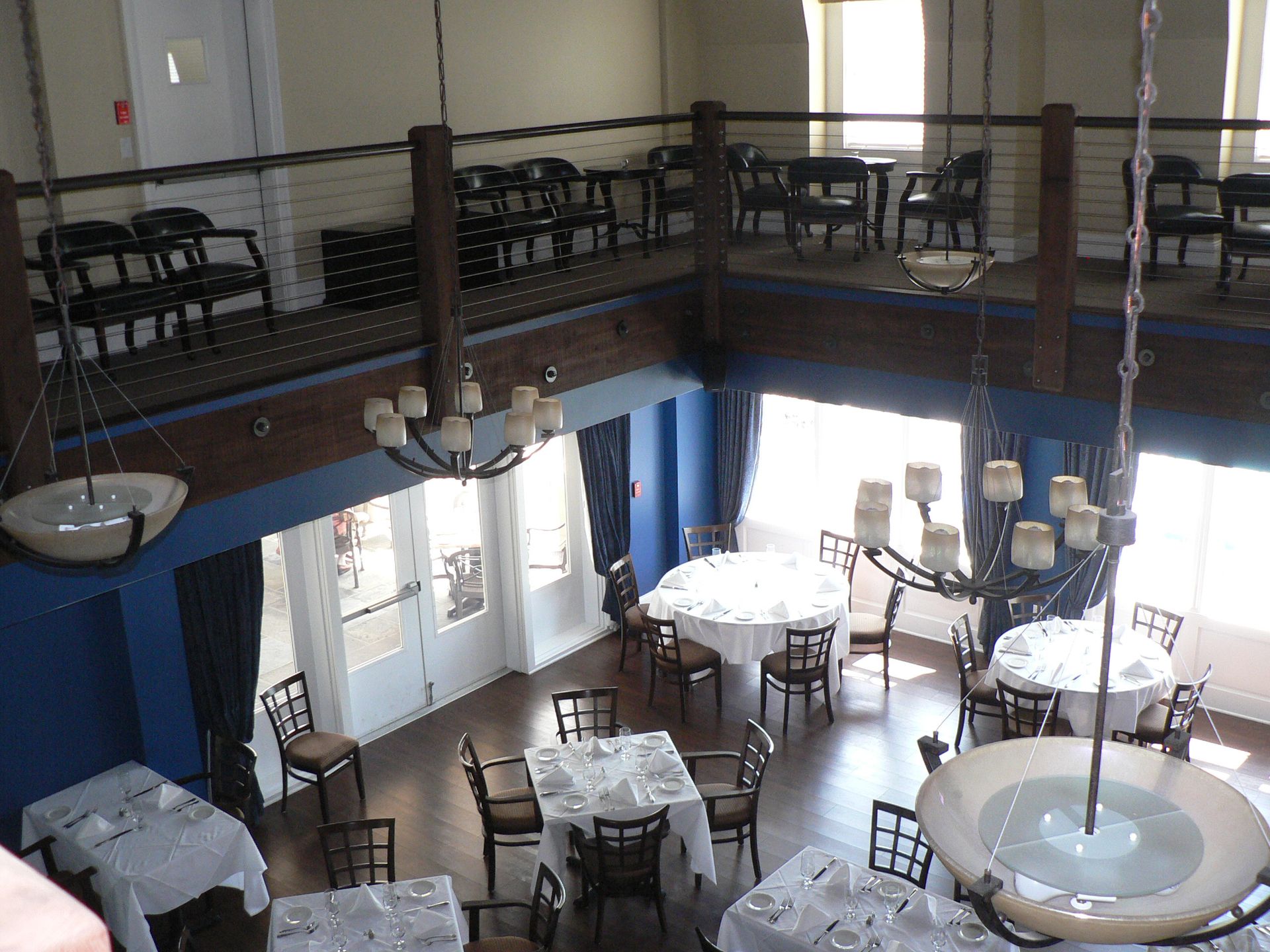 An elevated view of a dining room with round tables, chairs, chandeliers, and a balcony.