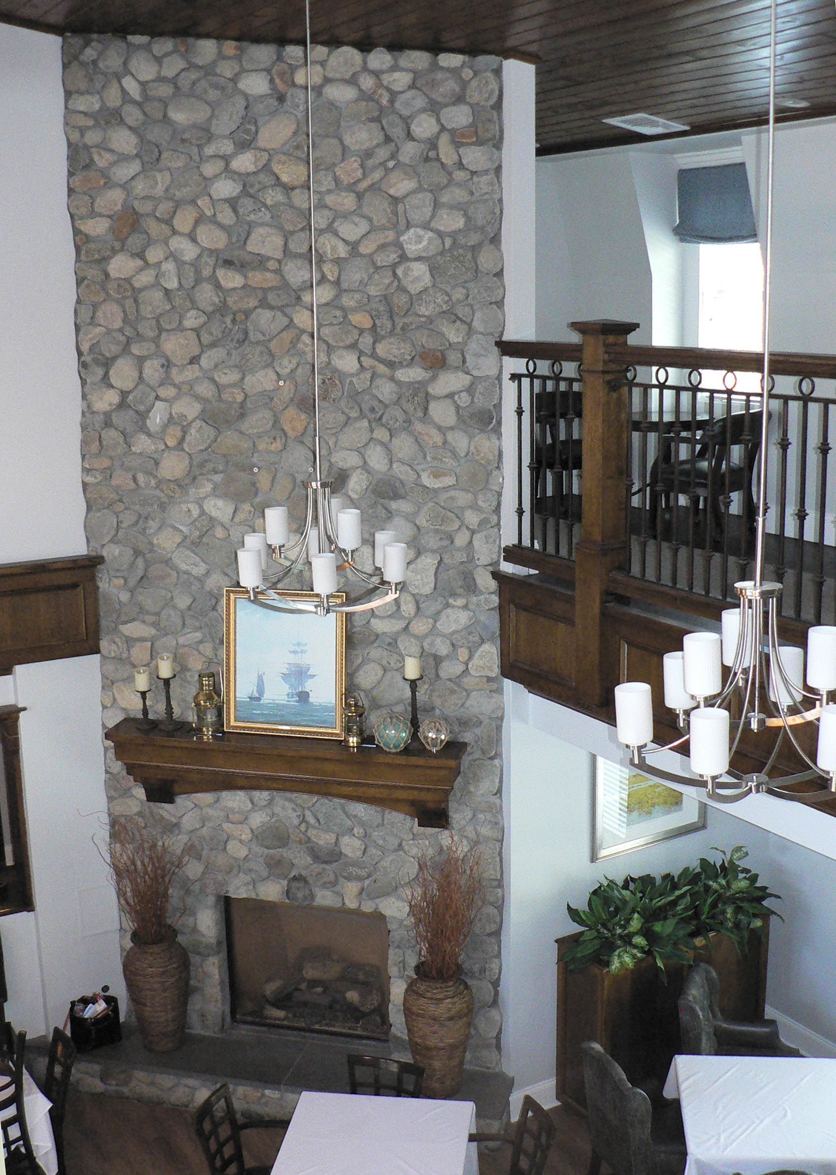 Interior view of a stone fireplace, with a dark wooden mantel, and a second-story balcony.