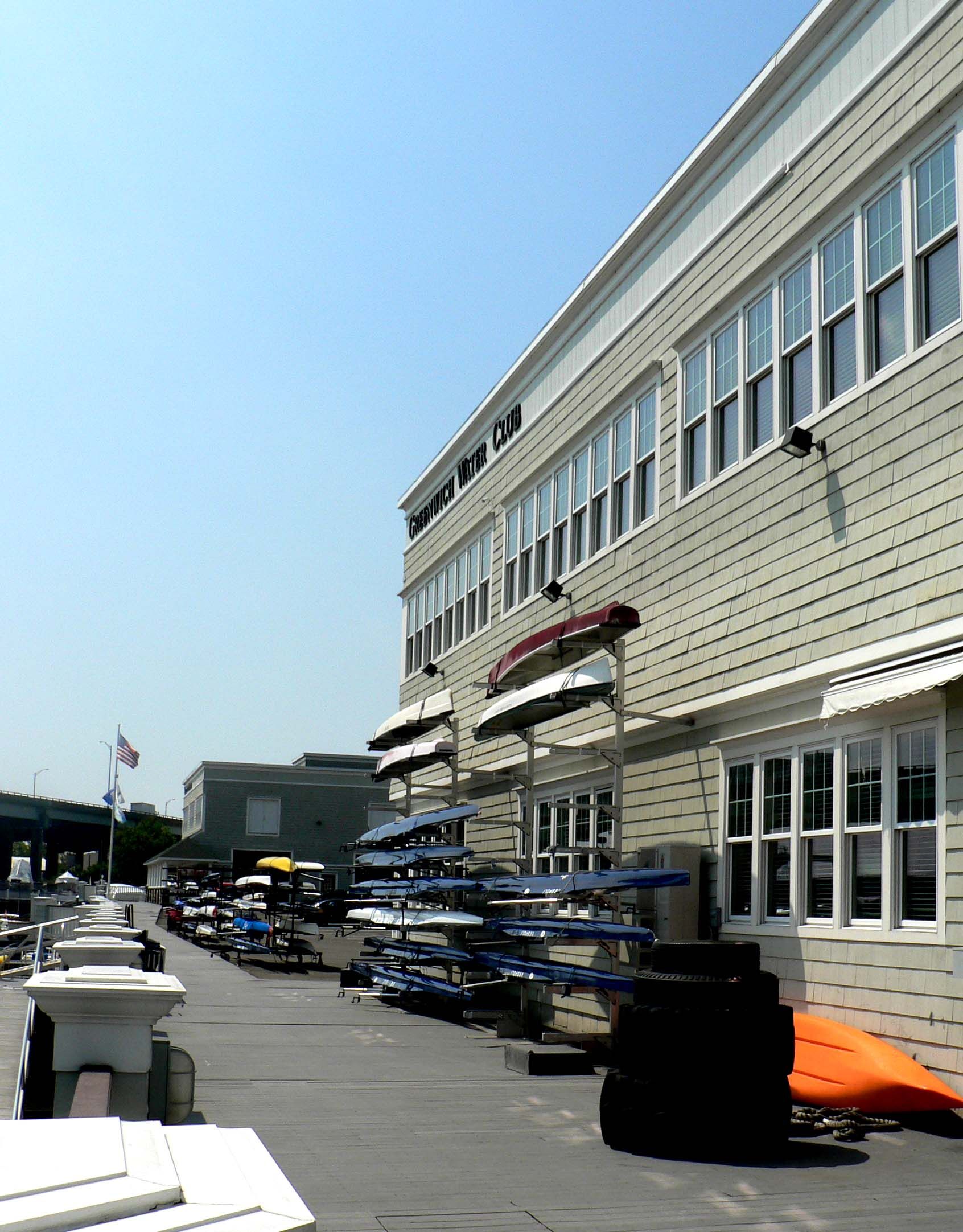 Building exterior with many windows, awnings, and racks of blue paddles on a sunny day.