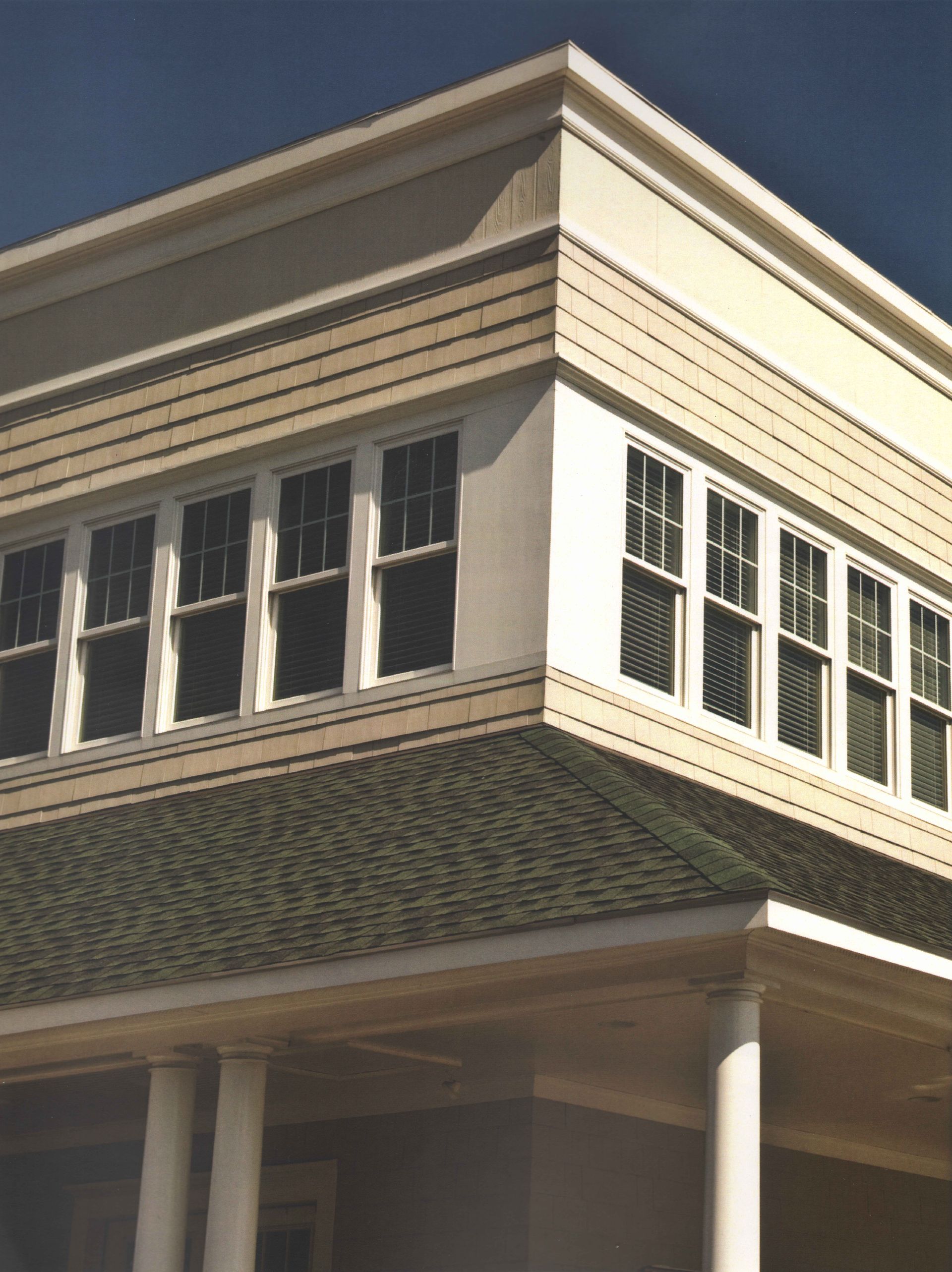 Corner of a two-story building with multiple windows, cream trim, and a green tile roof.