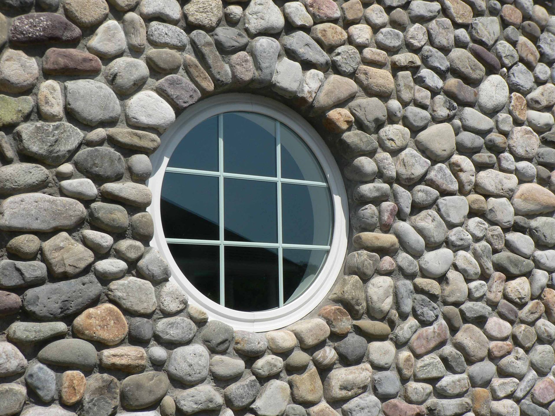 Round window in a stone wall, white frame with grid, exterior shot.