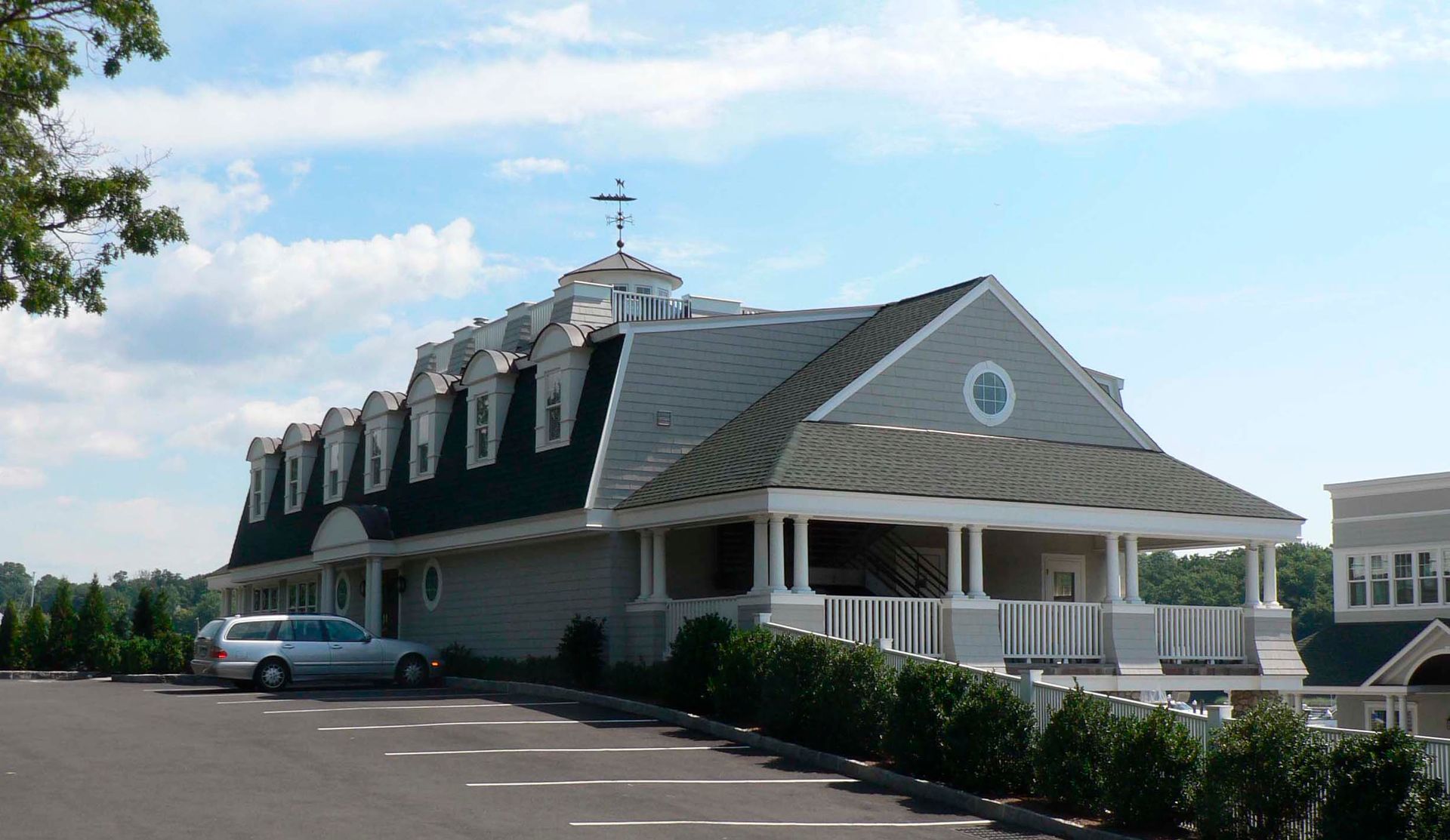A gray building with a unique roof design and dormer windows, parked car. Blue sky.