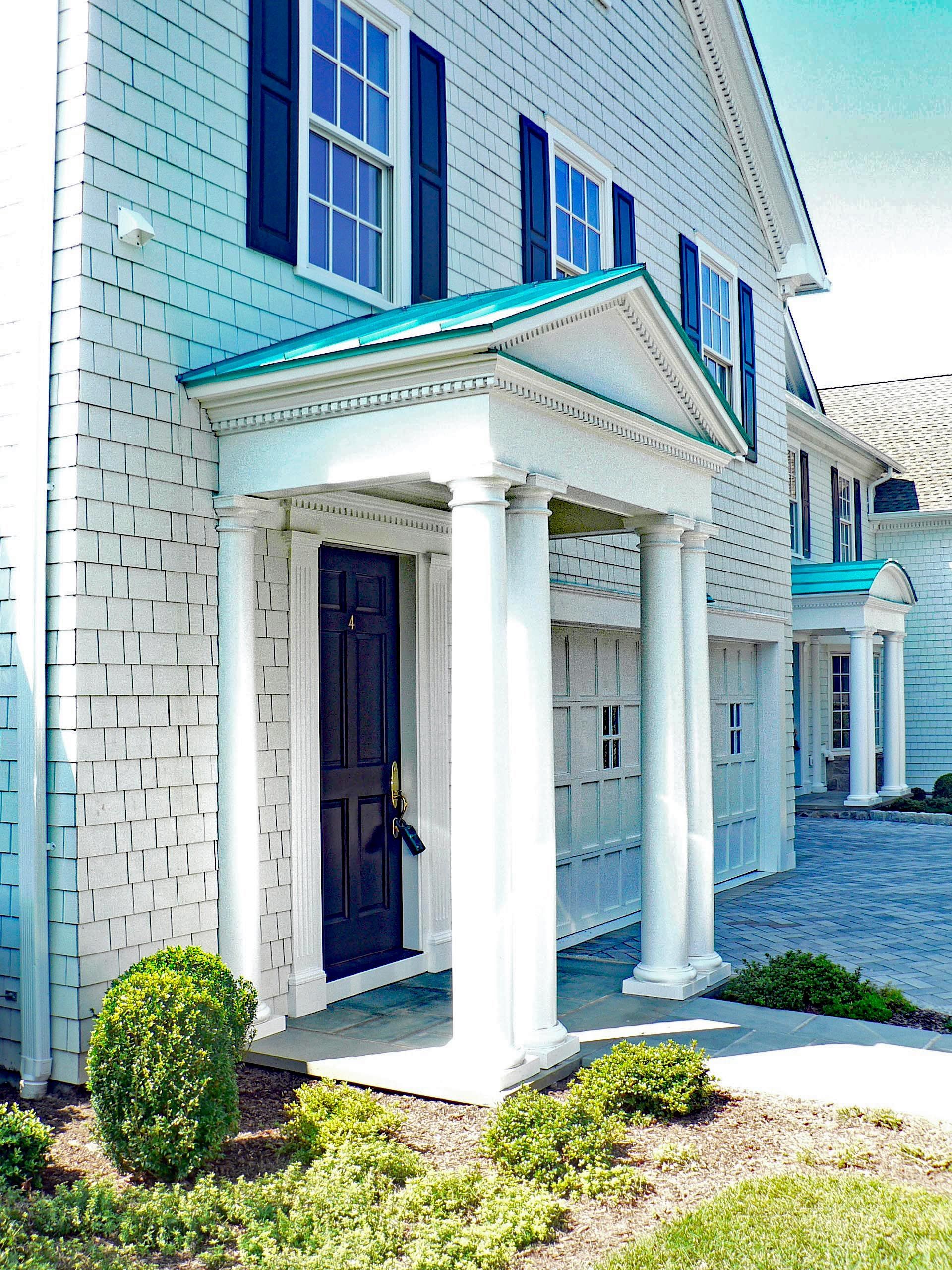 White clapboard building with a columned entrance, teal roof, and dark blue door.