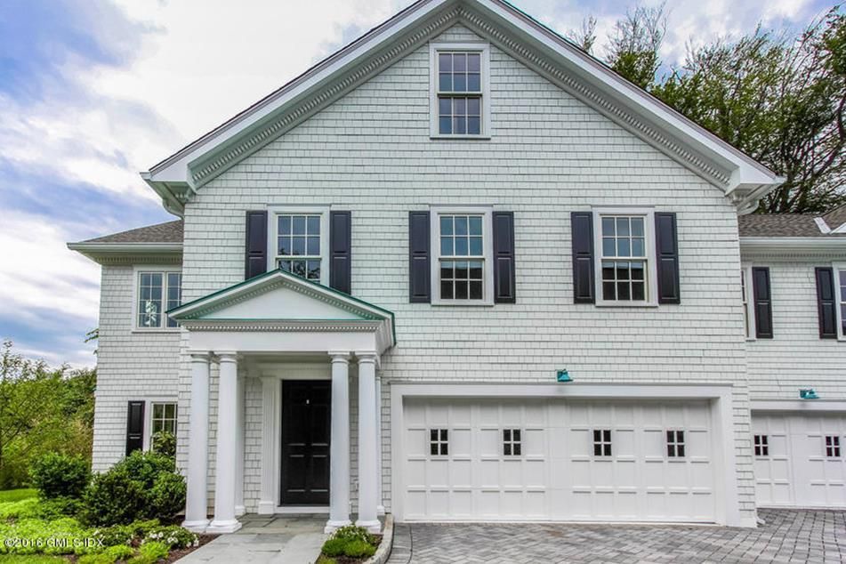 White house with black shutters, two-car garage, front door with columns, and a gray brick driveway.