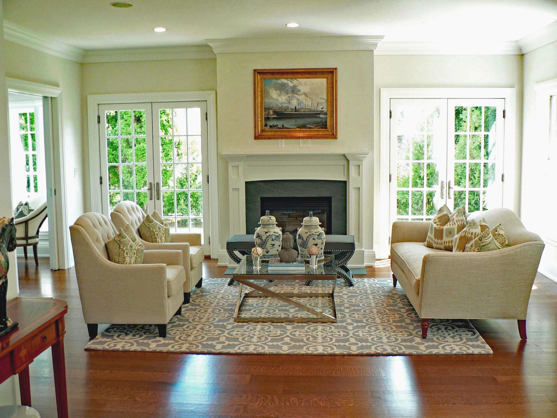 Living room with fireplace, cream-colored furniture, and glass doors with a view of greenery.